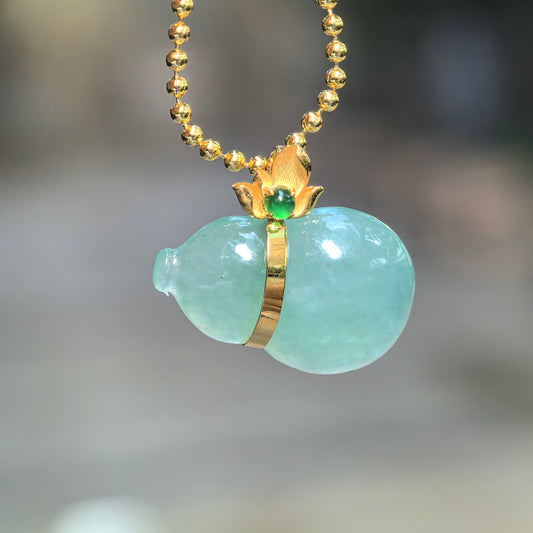 Icy green jadeite horizontal Gourd Pendant hanging from a chain, showing its rounded lobes, 18K gold waist band and floral bail with a green accent stone.