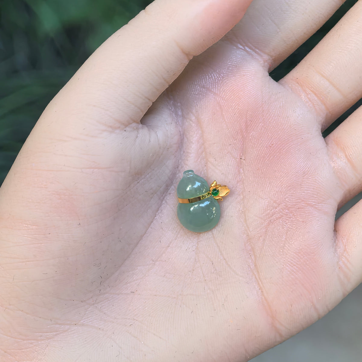 Green jadeite Gourd Pendant resting in an open palm, showing its compact proportions, polished surface and 18K gold setting.