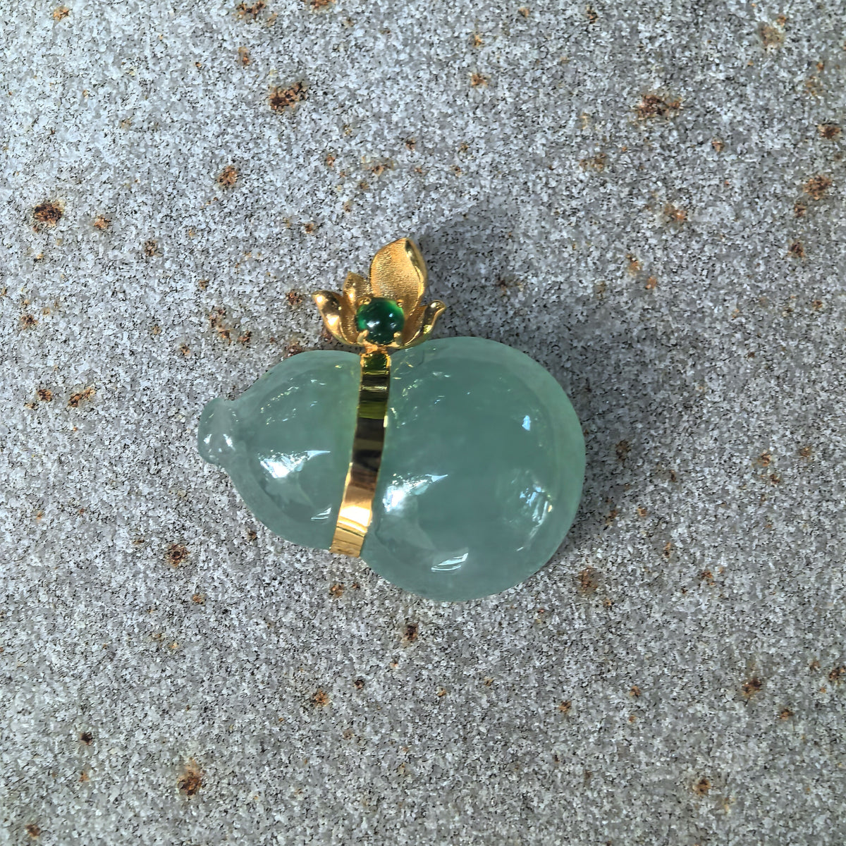 Front view of the icy green jadeite horizontal Gourd Pendant on stone, with an 18K gold band and a small green accent stone in the floral bail.