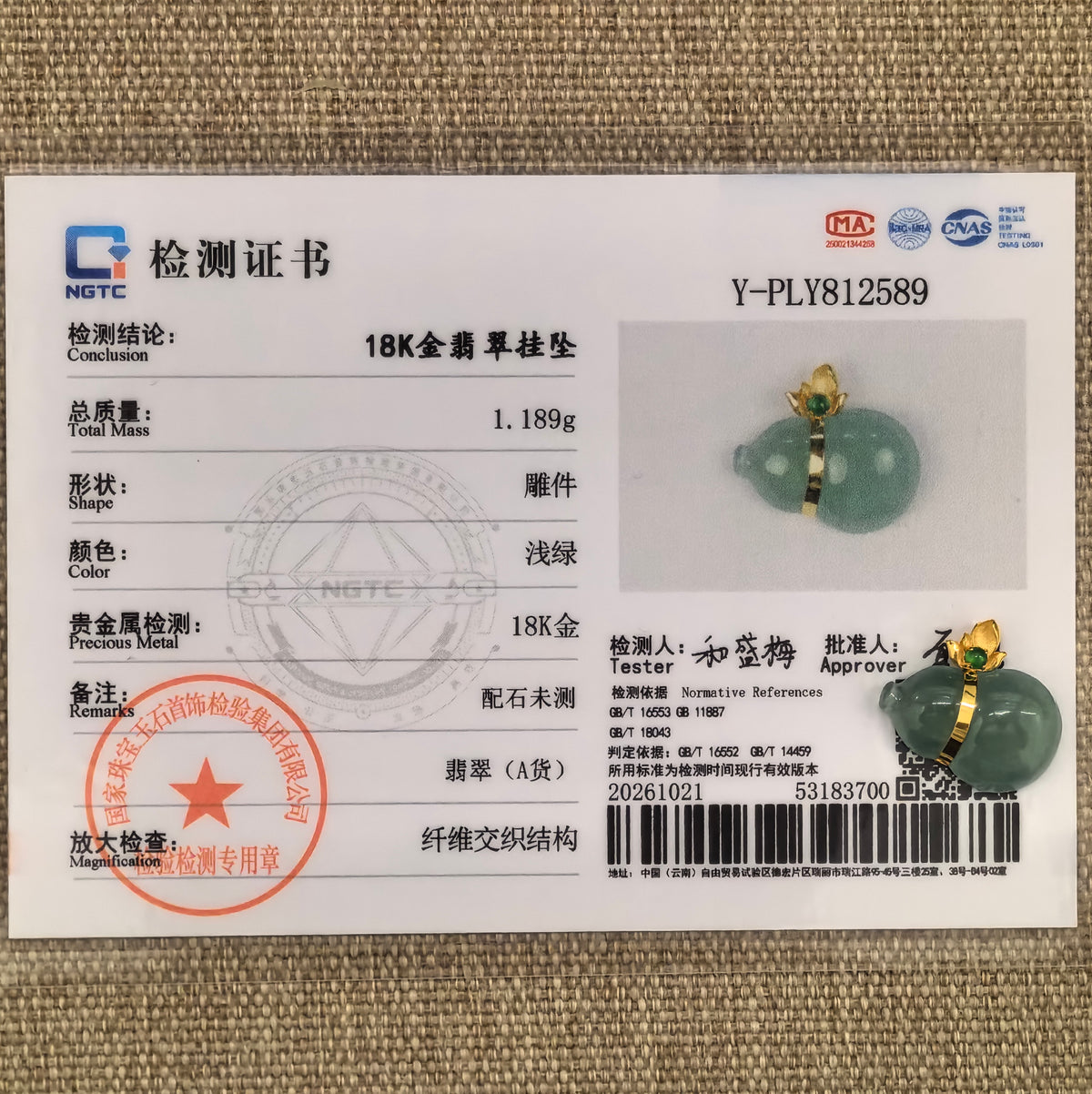 Green jadeite horizontal Gourd Pendant in 18K gold beside its matching NGTC certificate on woven fabric.