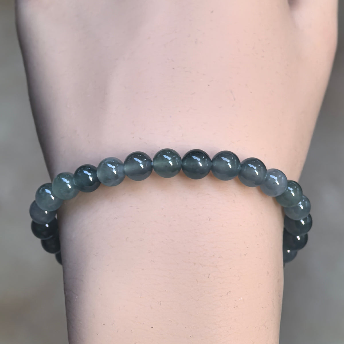 Front view of a deep green jadeite bead bracelet on the wrist, highlighting its simple continuous strand and rounded bead surfaces.