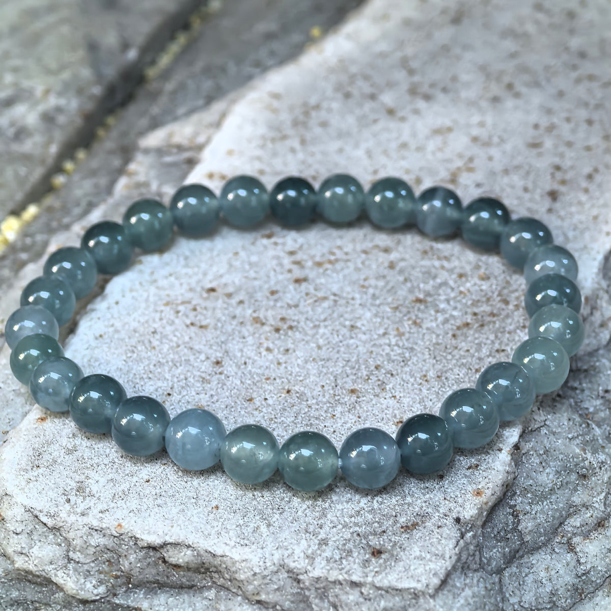 Angled view of a deep green Guatemalan jadeite bead bracelet arranged in a circle on a textured stone surface.