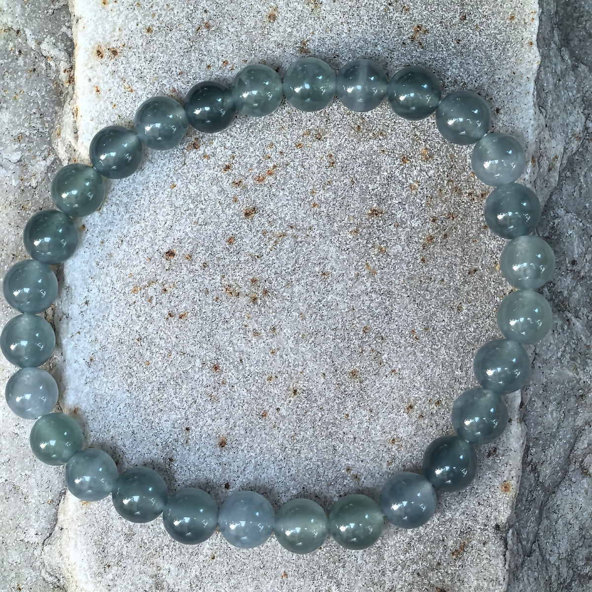 Overhead view of a deep green jadeite bead bracelet on stone, showing the full strand and variations in color between the round beads.