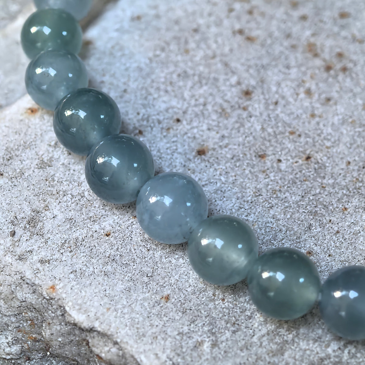 Close-up of icy glutinous deep green jadeite beads on stone, showing translucency, internal texture and lighter green areas.