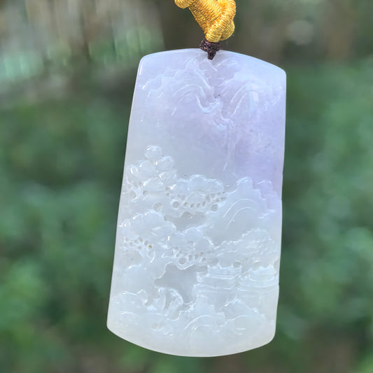 Glutinous jadeite landscape plaque pendant with purple coloring across part of the stone, hanging from a dark cord against a green background.