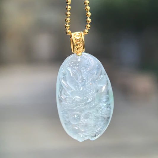 Icy white jadeite dragon pendant hanging from a chain, showing its oval relief carving and decorative 18K gold bail.