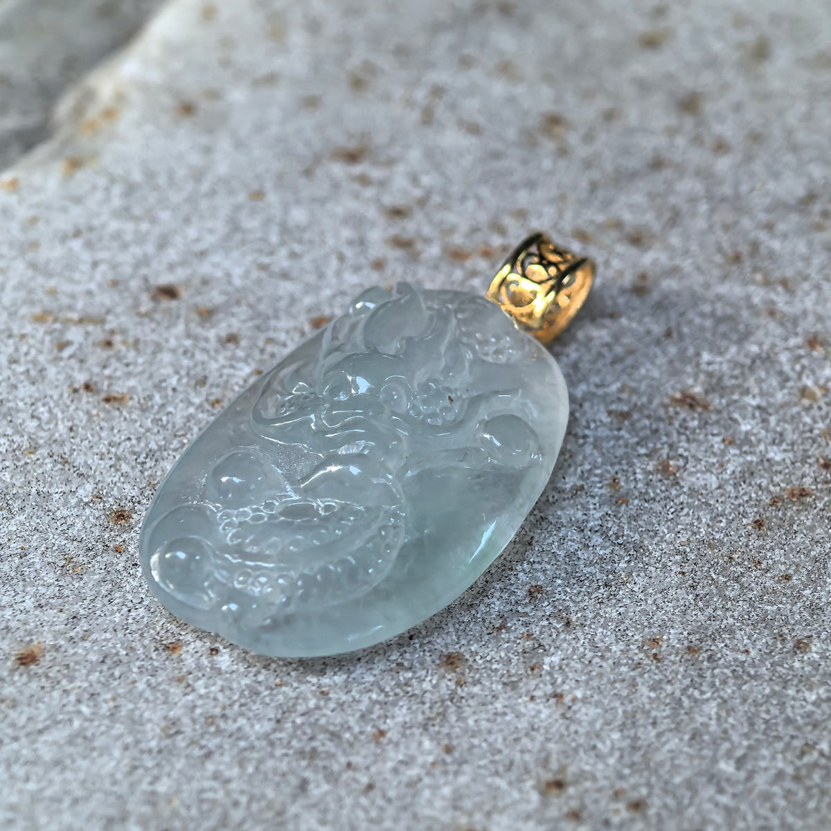 Angled close-up of an icy white jadeite dragon pendant on stone, highlighting the raised face, scaled body and rounded orb motif.