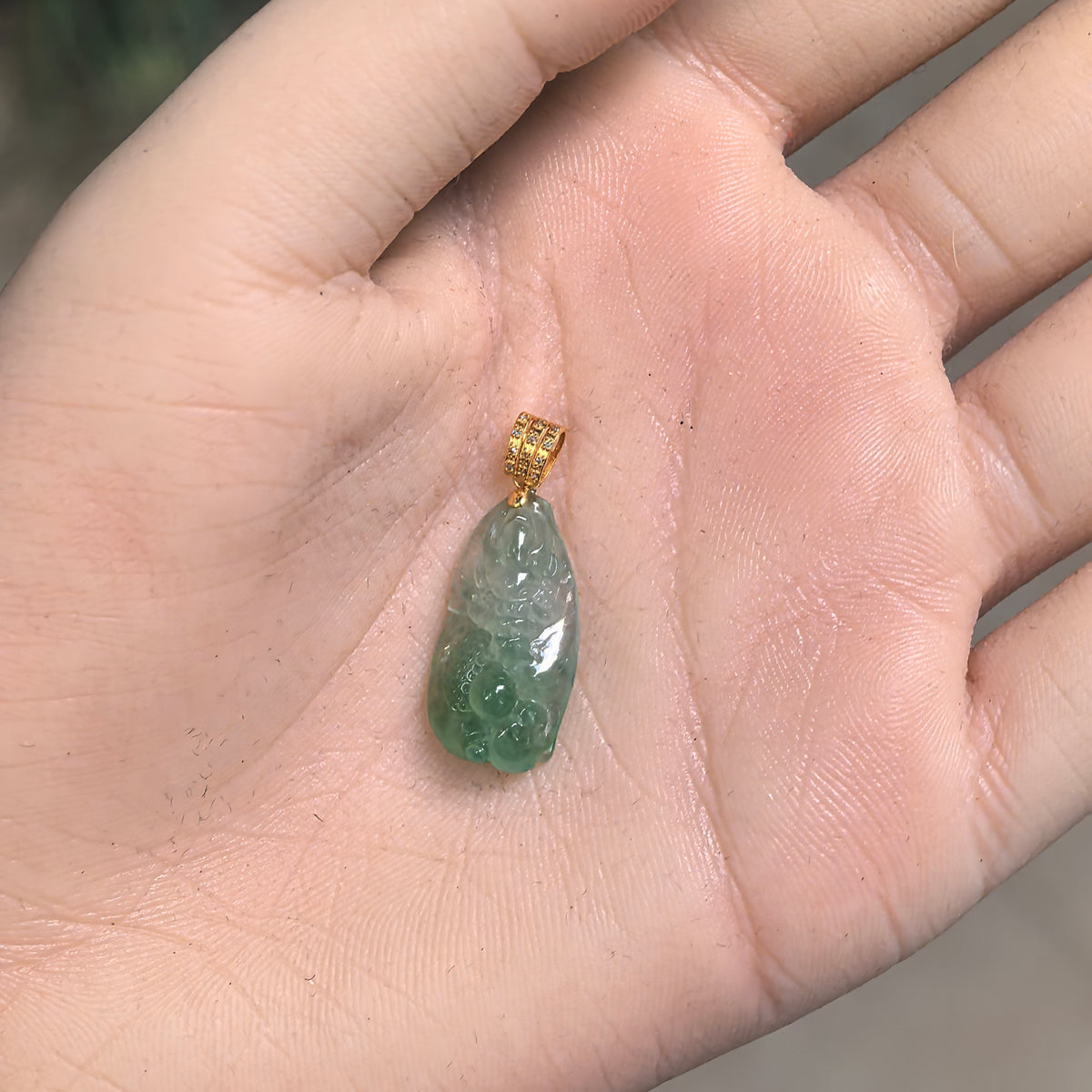 Light green jadeite dragon pendant resting in a palm, showing its compact elongated shape and deeper green lower section.