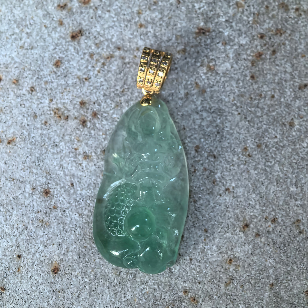 Front close-up of a light green jadeite dragon pendant on stone, showing the dragon’s face, curling body and deeper green accents.