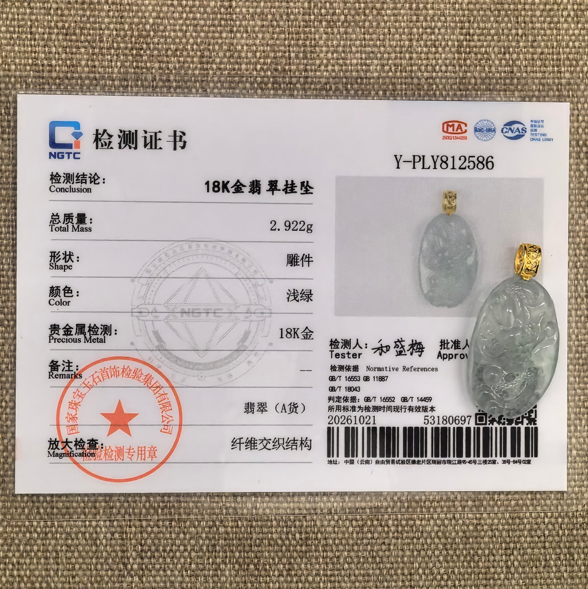 White jadeite dragon pendant with a subtle green undertone beside its matching NGTC certificate on woven fabric.