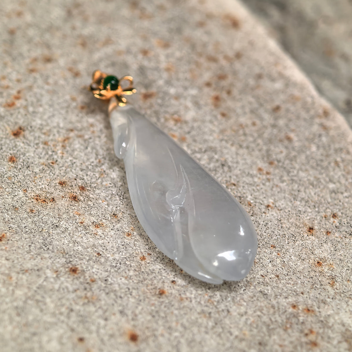 Angled view of the white jadeite Magnolia Pendant on stone, showing the curved petal carving and polished surface.