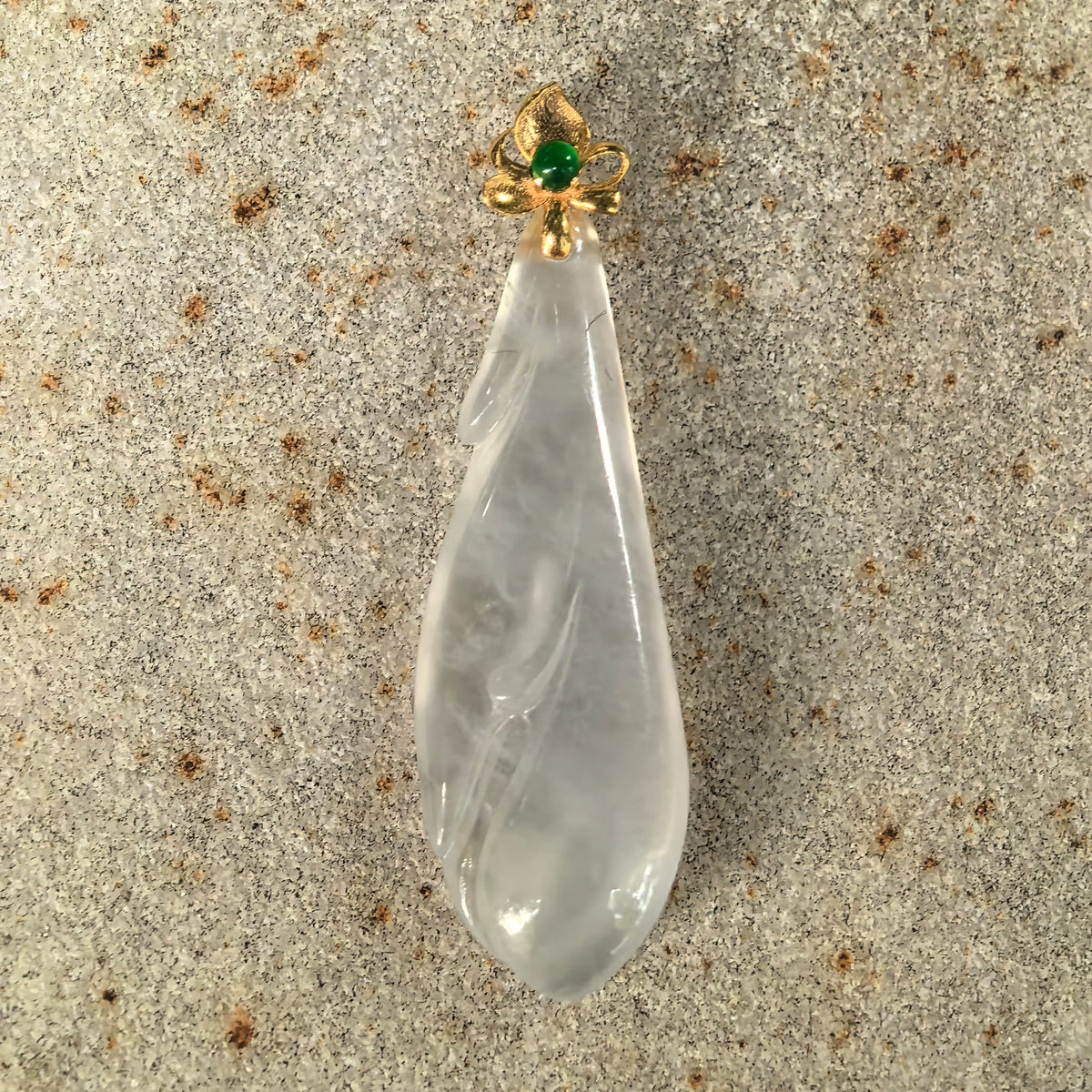 Front close-up of the icy white jadeite Magnolia Pendant on stone, showing its elongated flower shape and gold floral bail with a green accent.