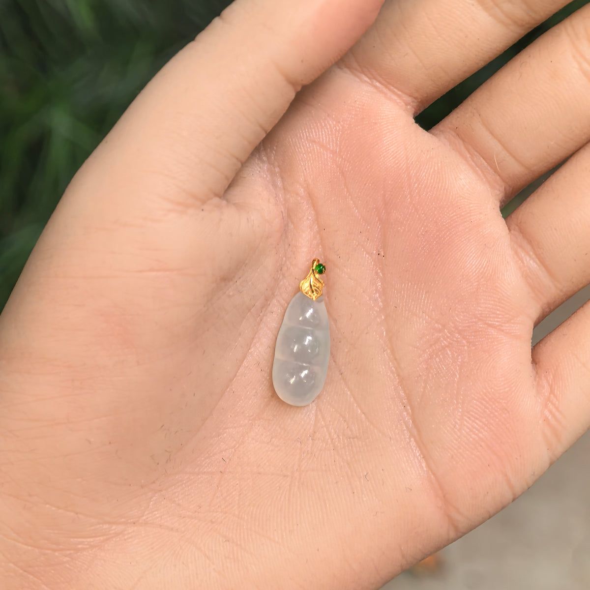 Pale green jadeite Bean Pod Pendant resting in a palm, showing its petite proportions and rounded bean carving.