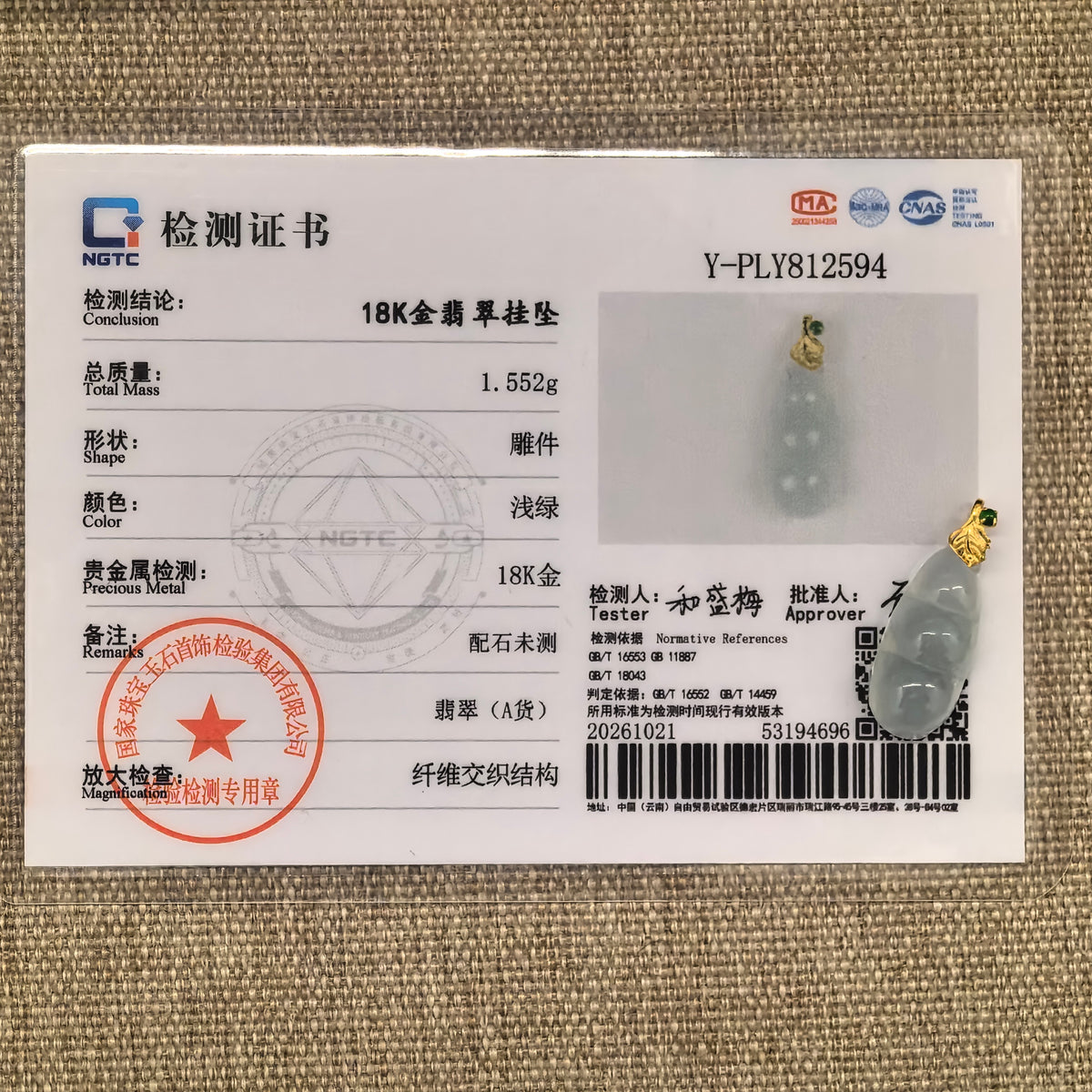 Pale green jadeite Bean Pod Pendant with an 18K gold leaf bail beside its matching NGTC certificate on woven fabric.