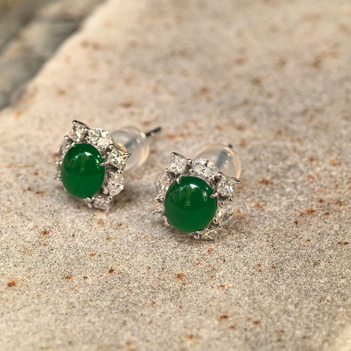 Angled view of the green jadeite stud earrings on stone, showing the domed cabochons, natural diamond halos and raised 18K gold settings.
