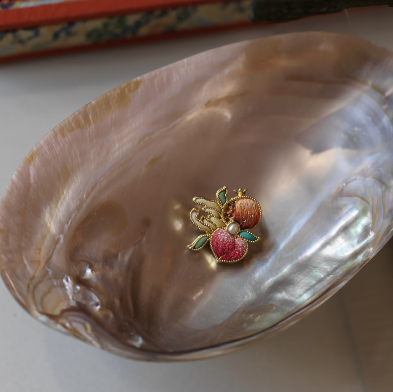 Suzhou silk embroidery brooch pendant resting in a mother-of-pearl shell, showing natural silk and gold-thread embroidery details.