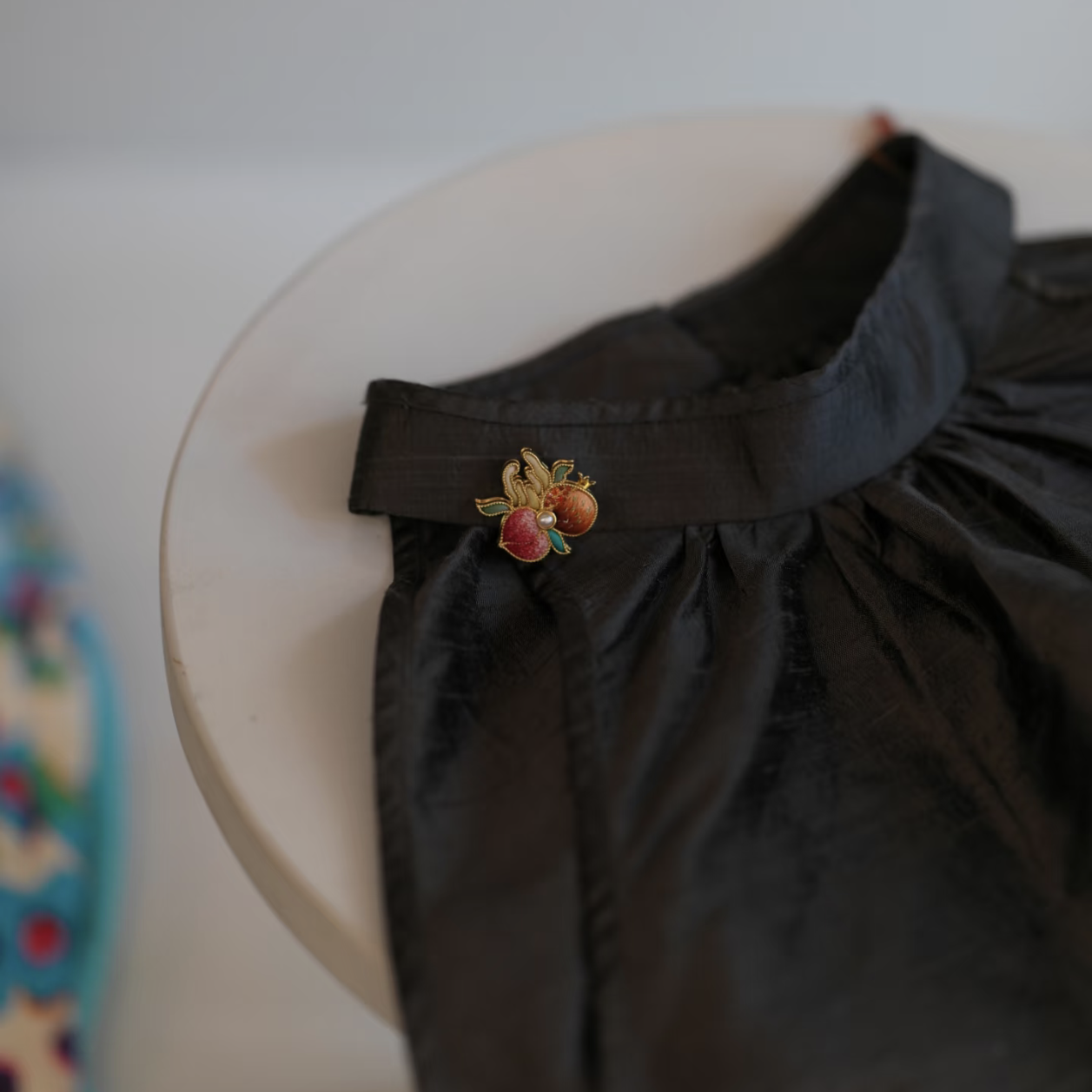 Suzhou embroidery Three Blessings brooch pinned to a black garment, featuring pomegranate, Buddha’s hand citron and longevity peach motifs.