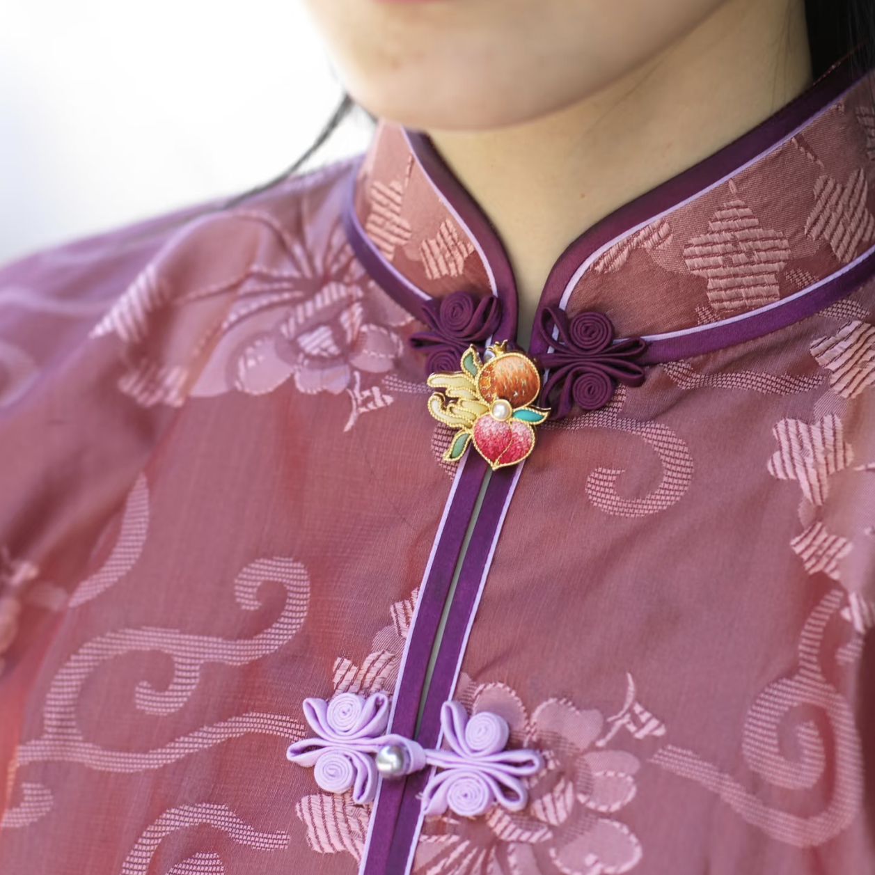 Suzhou silk embroidery brooch worn at the collar of a rose-purple qipao as a traditional Chinese jewelry accent.