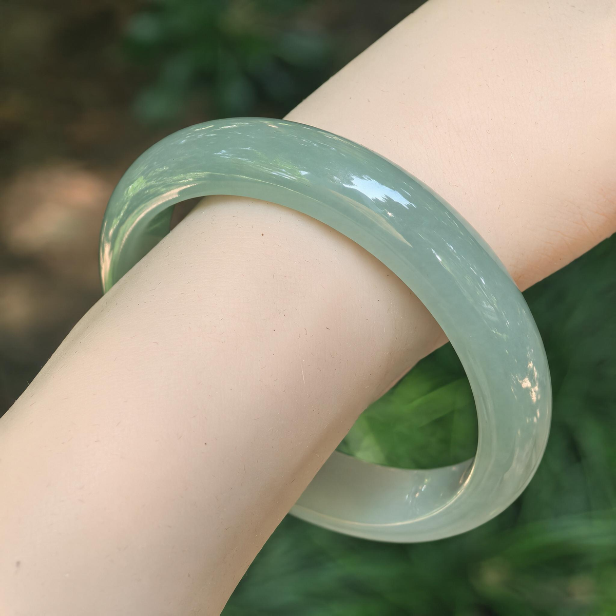 Angled wrist view of a light green jadeite D-shape bangle, showing its smooth curves and soft translucent appearance.