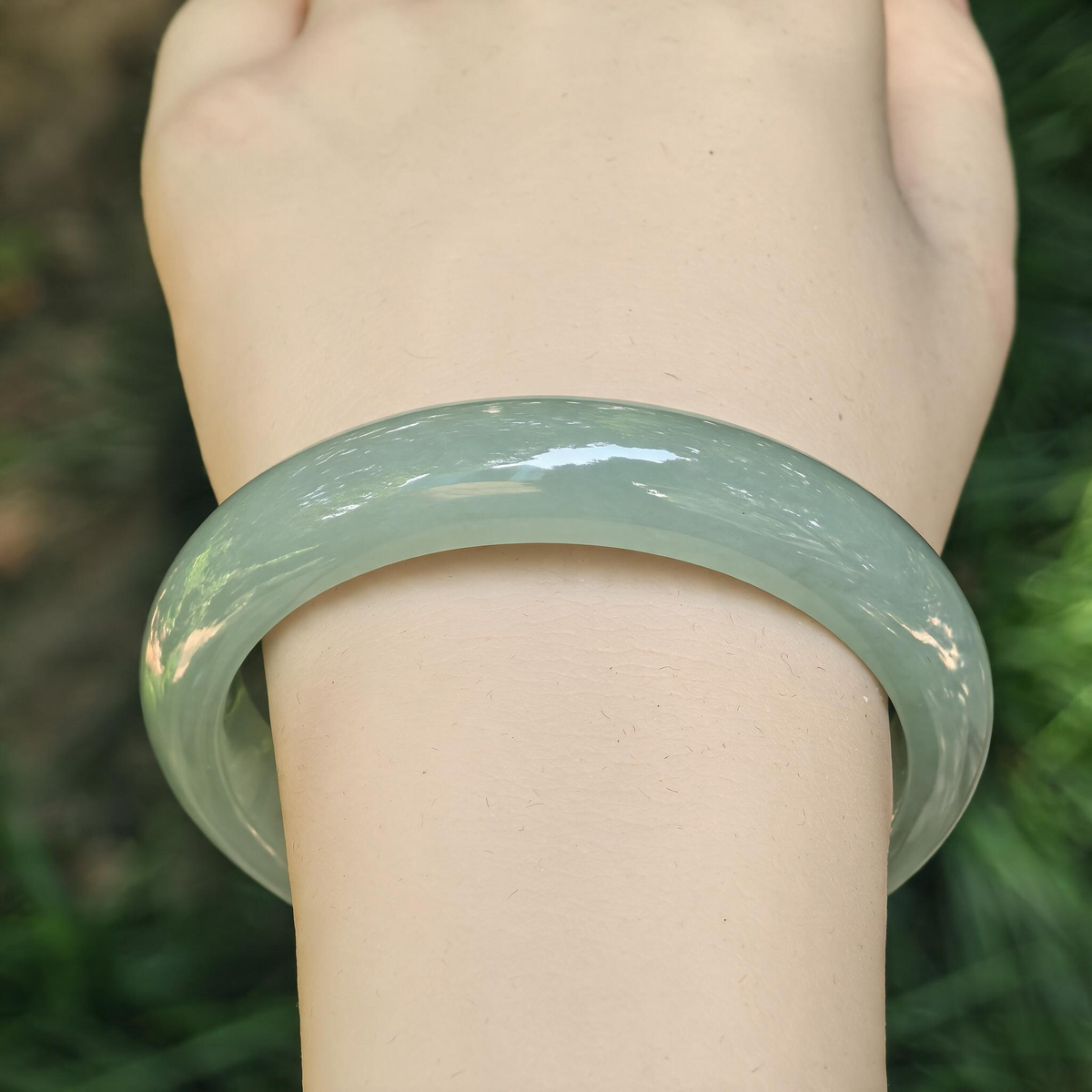 Front wrist view of a light green icy glutinous jadeite D-shape bangle, showing its even color and polished rounded outer surface.
